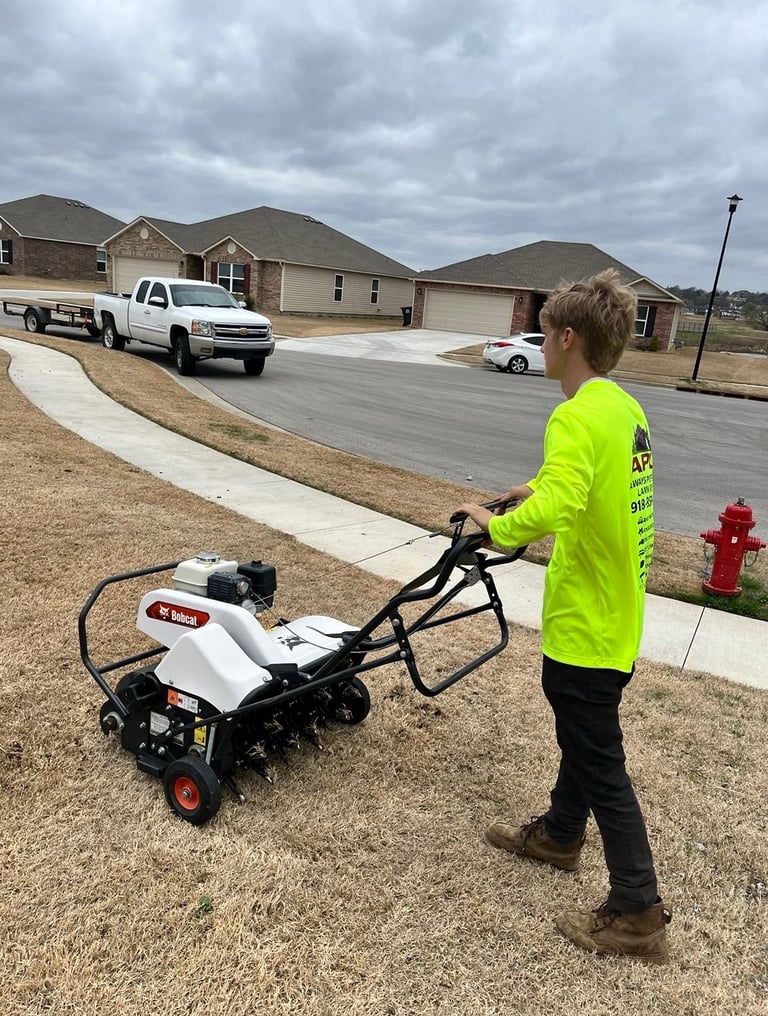 Person in yellow safety vest operating a walk-behind tiller machine on driveway with residential home and vehicles in background